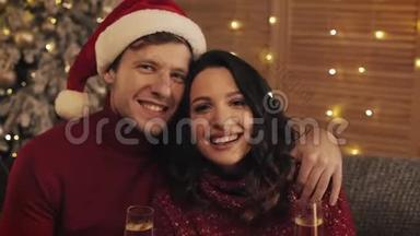 温馨舒适的家居氛围中，幸福的微笑情侣捧着香槟欢乐的酒杯坐在圣诞树附近